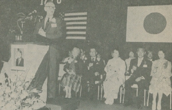 Mike Mansfield addresses a huge assembly of Americans and their guests in defining the pride of Americans feel in their past and their confidence in the future. Behind, Mrs. Mansfield, HIH Prince and Princess Hitachi.