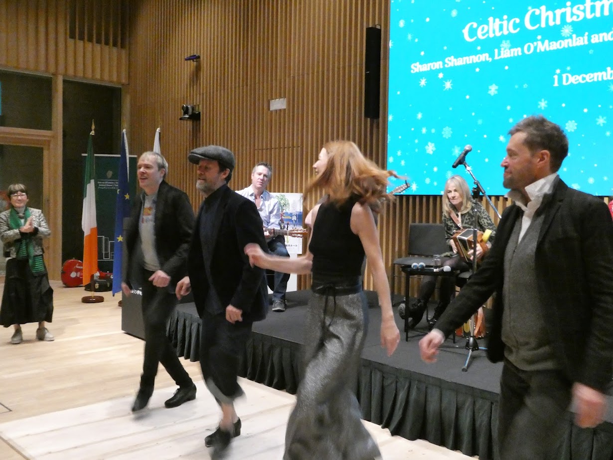 Traditional Irish dancers performing a high-energy routine on a wooden stage at the Irish Embassy in Tokyo.