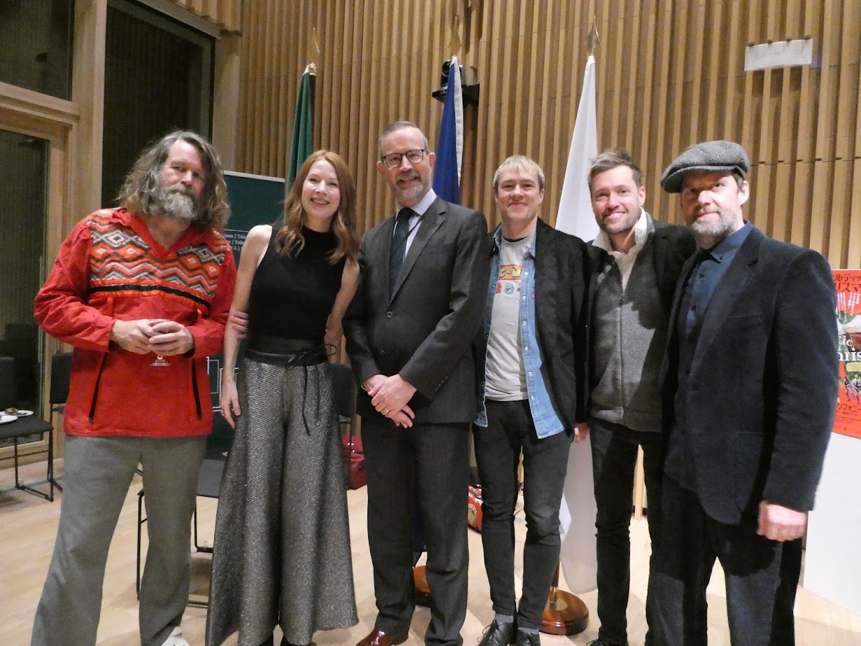 A group photo of the Celtic Christmas 2025 performers standing between the Irish and Japanese flags at Ireland House.