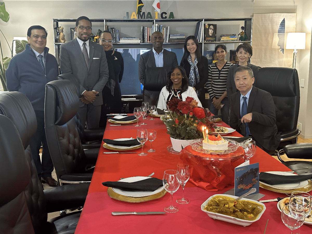 Ambassador Shorna-Kay Richards and the Jamaican Embassy staff gathered around a dining table with a cake, celebrating their collective efforts in Japan.