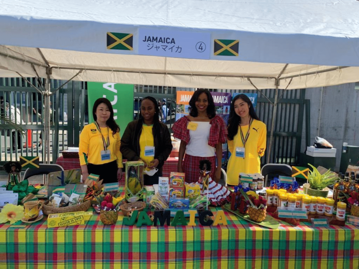 Ambassador Shorna-Kay Richards and embassy staff at a "Brand Jamaica" festival booth in Japan, showcasing Jamaican products, Blue Mountain coffee, and cultural exports.