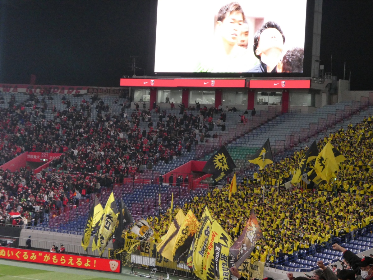 Kashiwa Reysol supporters raising yellow flags during the match against Urawa Reds at Saitama Stadium.