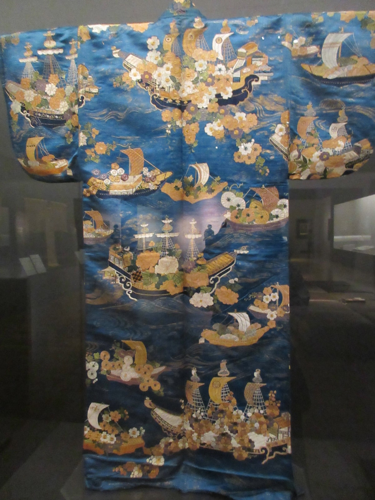 An intricate blue silk kimono featuring detailed embroidery of sailing ships and floral patterns.