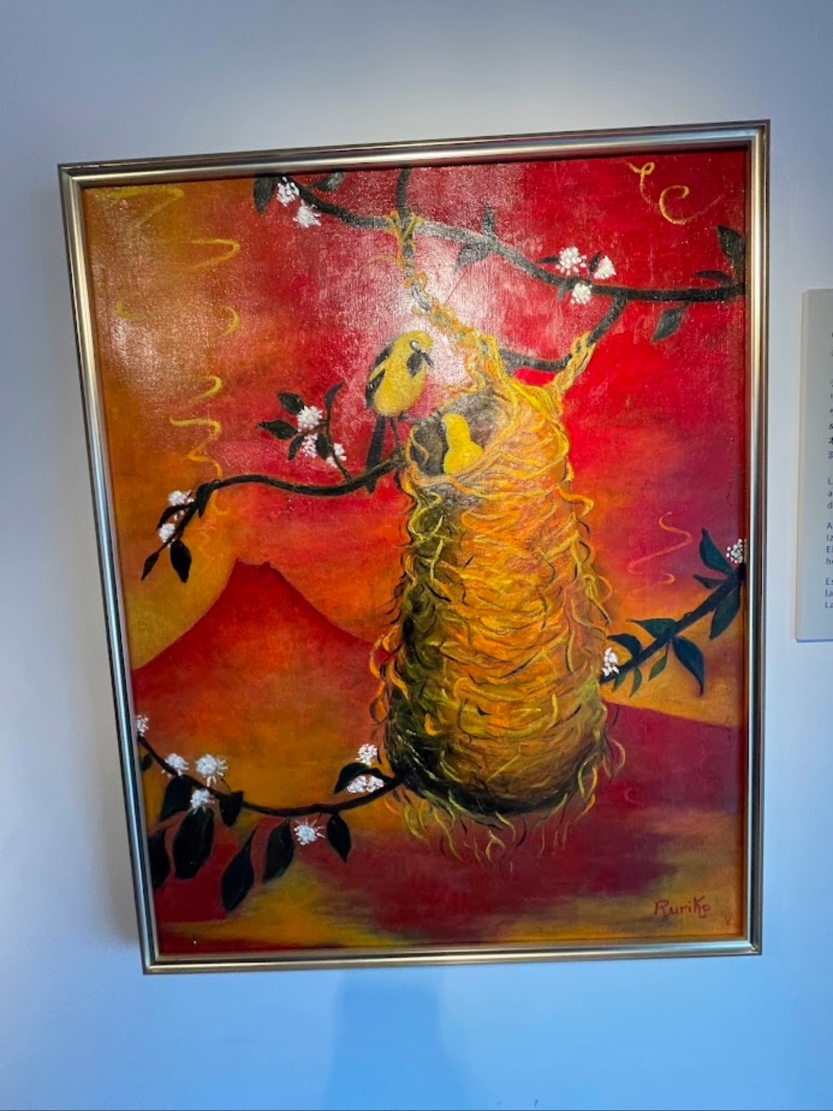 An oil painting by Ruriko Escobar depicting yellow birds in a nest against a warm, mountainous landscape, symbolizing the fertility of Salvadoran land.