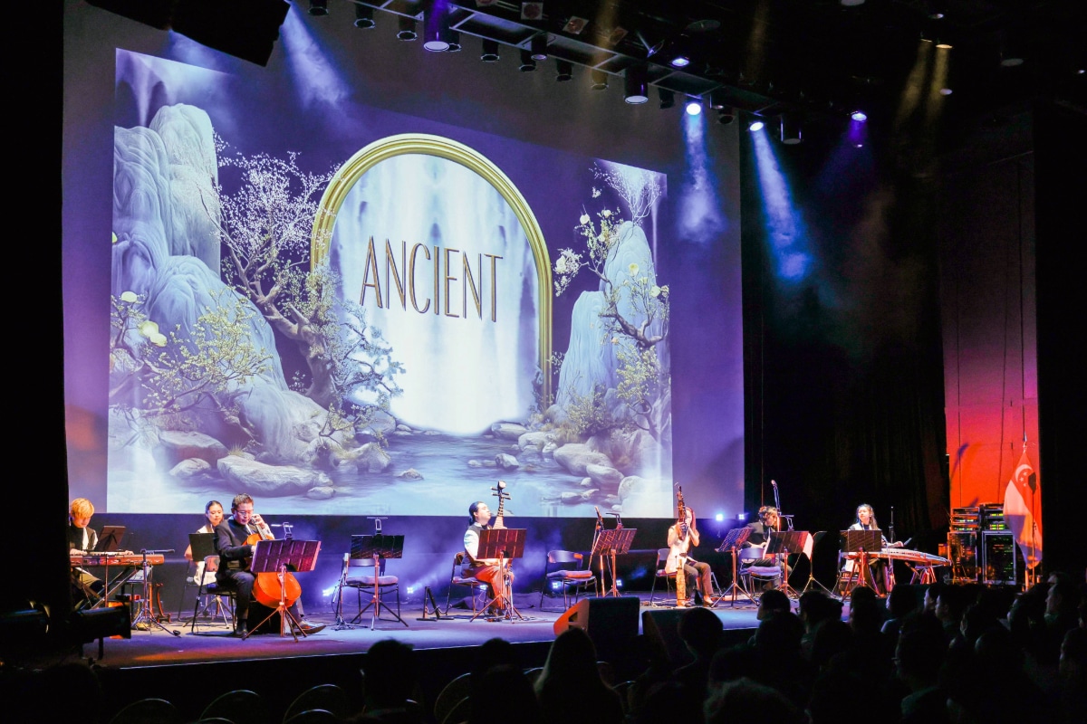 Members of the TENG Ensemble performing with a mix of traditional and modern instruments against a scenic "Ancient" themed digital background.