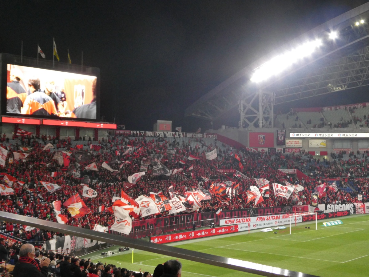 Urawa Reds fans waving flags and supporting their team at Saitama Stadium.