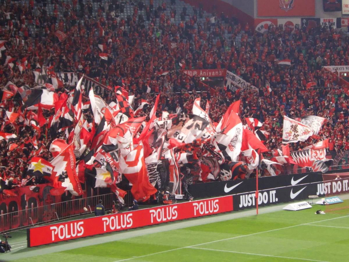 Urawa Reds fans waving red flags in the stands, showcasing the passionate atmosphere of Japanese football.