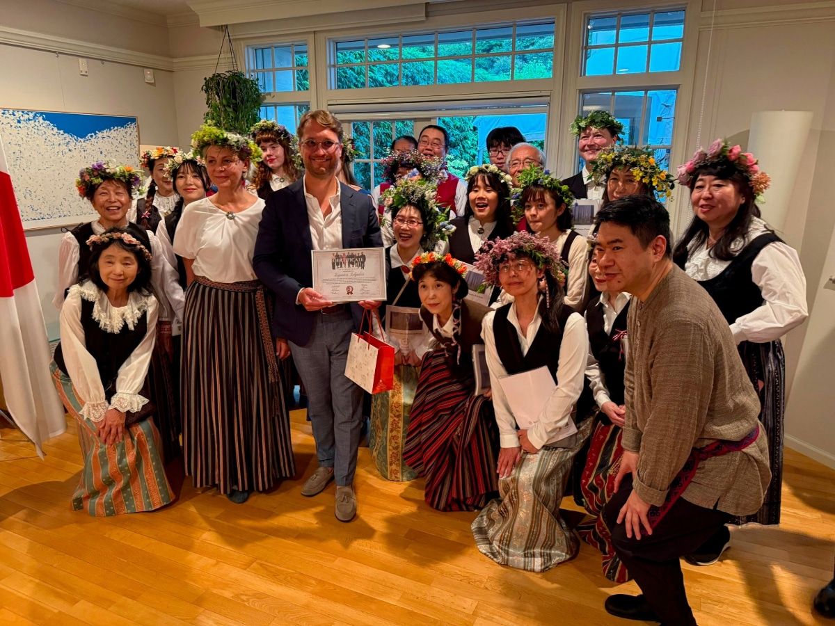 民族衣装を身にまとった合唱団「ガイスマ」のメンバーが、証書を手にしたズィルガルヴィス大使と共に記念撮影。