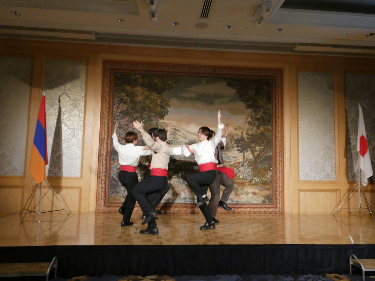 Dancers in white shirts and red sashes perform between the Armenian and Japanese flags at the Independence Day reception