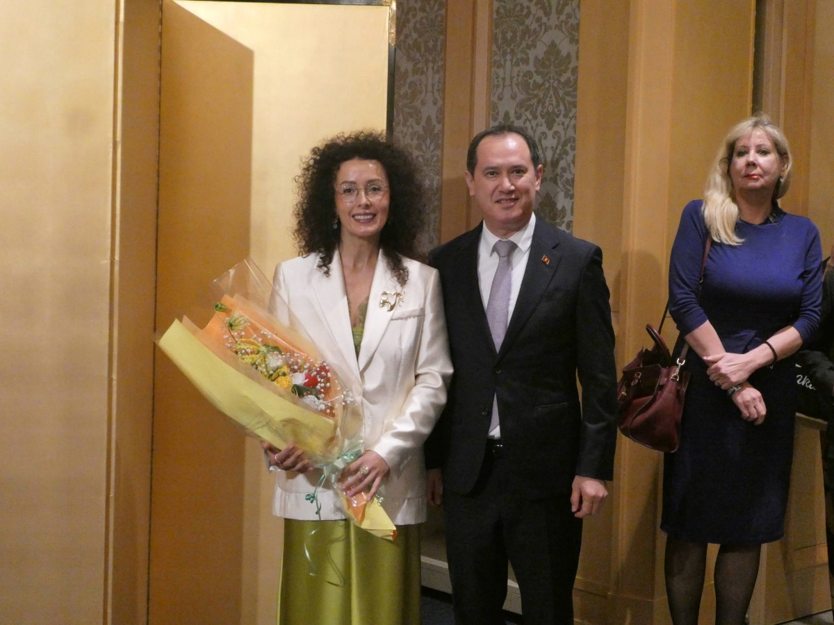 A woman in a white jacket holding a bouquet poses with a man in a dark suit at the Armenia Independence Day reception