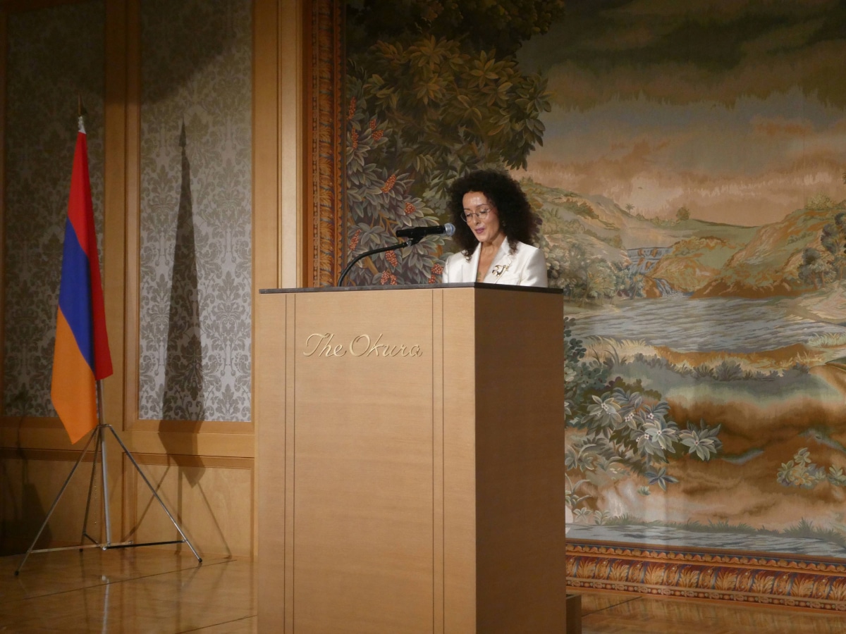 アルメニア独立記念日レセプションで、アルメニア国旗の横の演台で挨拶する白いジャケット姿の女性