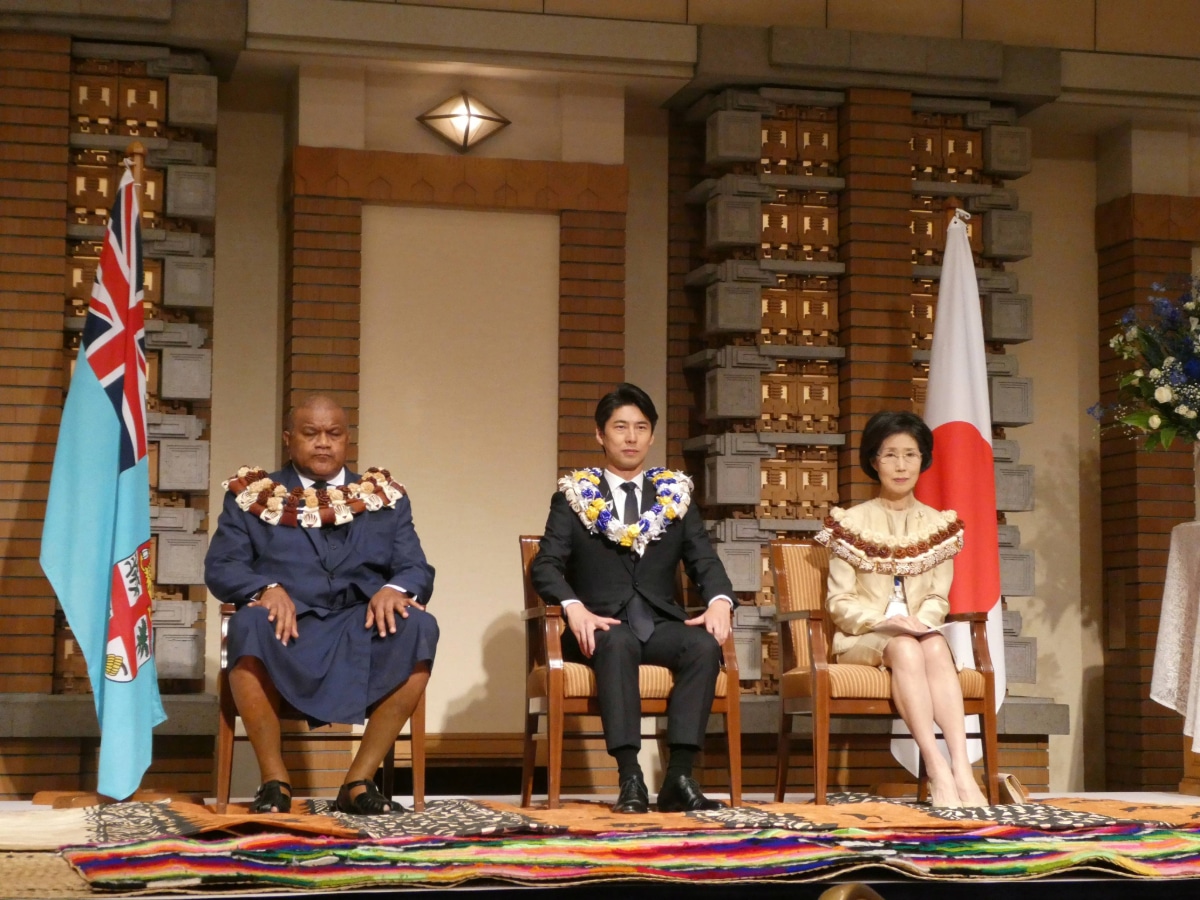 フィジーデーレセプションのステージで、フィジーと日本の国旗の間に着席する3名の来賓