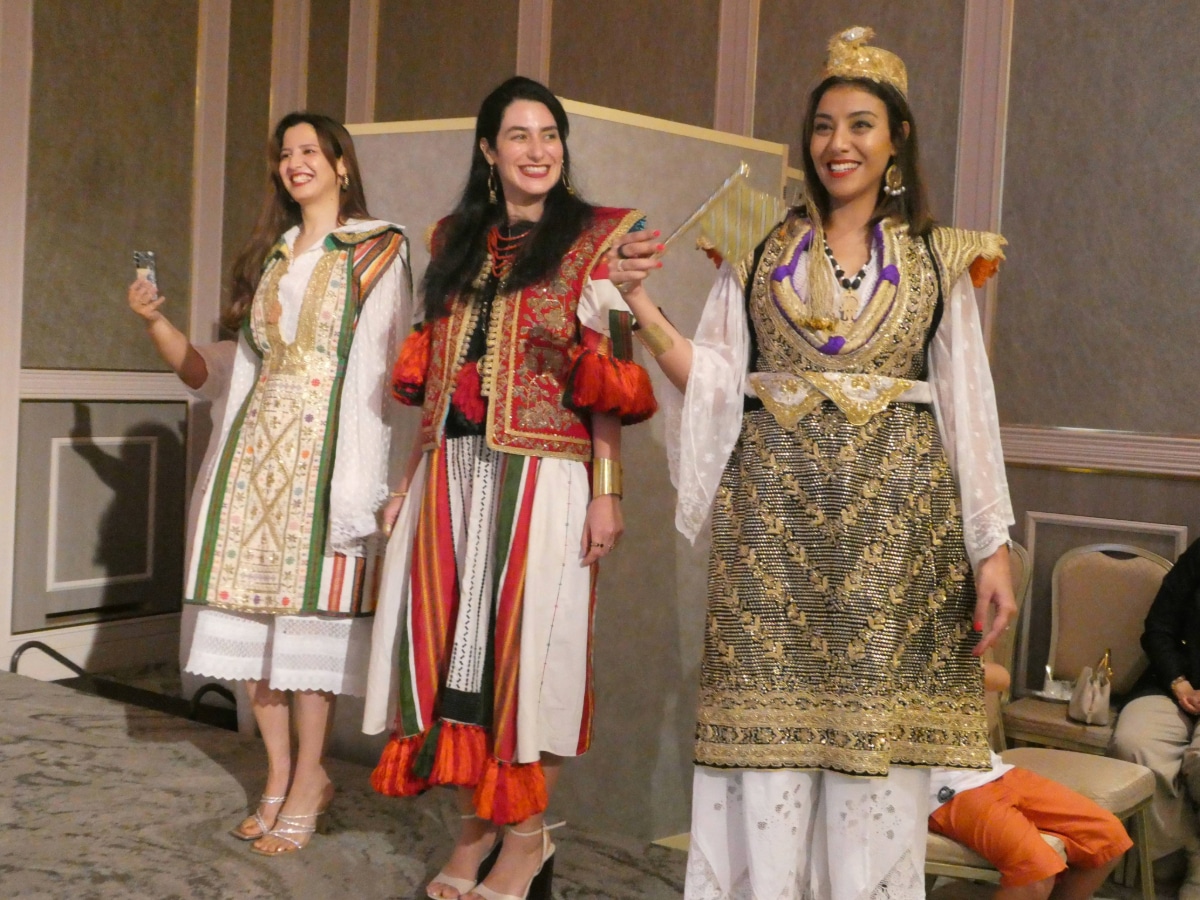 Three smiling women wearing embroidered traditional Tunisian dresses at the anniversary reception